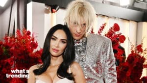 Megan Fox and Machine Gun Kelly posing together in front of red floral arrangements at an event