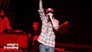 Young male rapper wearing a red cap and plaid shirt performing on stage with a microphone and all-access pass.