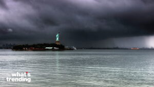 Statue of Liberty on Liberty Island with dark storm clouds and rain over New York Harbor.