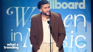 Bad Bunny speaking at the Billboard Women in Music event wearing a brown blazer and beige pants.