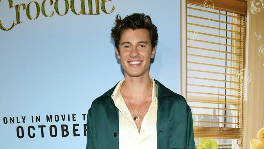 Shawn Mendes smiling at the Crocodile Dundee movie event with a green jacket and cream shirt