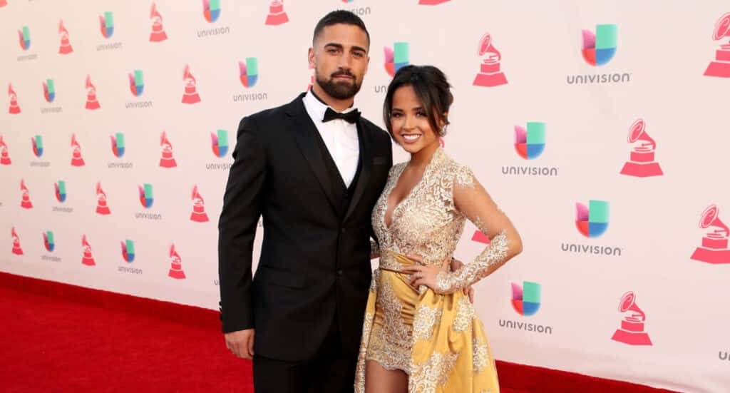 Man in black tuxedo and woman in gold and lace dress posing on the red carpet at a Univision Latin Grammy event
