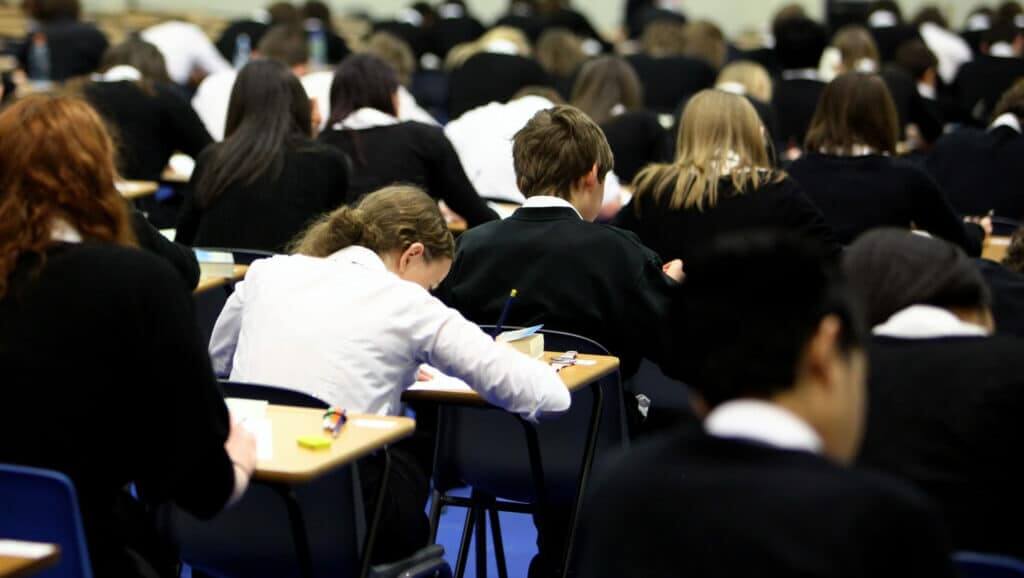 Students in black and white uniforms sitting at desks taking an exam in a large classroom