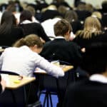 Students in black and white uniforms sitting at desks taking an exam in a large classroom
