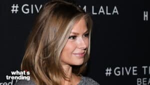 Woman with long blonde hair smiling against a black backdrop with "#GIVE" text visible