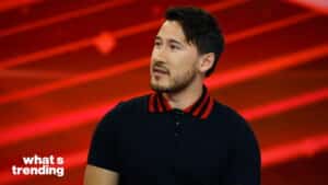 Markiplier speaking on the set of What's Trending with a red background and black shirt with red collar stripes