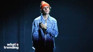 Justin Bieber wearing an orange beanie and blue checkered jacket holding a microphone on stage