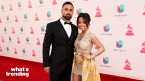 Man in black tuxedo and woman in gold lace dress posing on red carpet at Univision event
