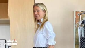 Gwyneth Paltrow wearing a white blouse and patterned skirt standing indoors near a clothing rack.