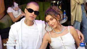Justin Bieber wearing black sunglasses and white hoodie sitting next to Hailey Bieber in a white tank top and diamond necklace