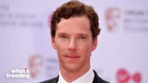 Benedict Cumberbatch in a black suit and white shirt at a red carpet event with BAFTA logos in the background