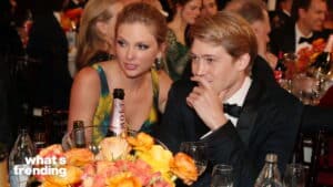 Taylor Swift and Joe Alwyn seated at a formal event table with flowers and Moët champagne bottle.