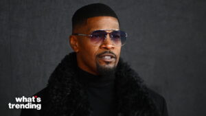 Jamie Foxx wearing sunglasses and a black fur coat against a dark background with "what's trending" logo