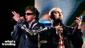 Two male musicians performing on stage, one with curly hair and sunglasses, the other with a shaved head holding microphones.