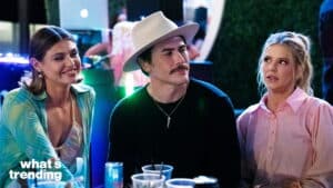 Three people sitting at a table with drinks, one man wearing a white hat and two women in casual outfits.