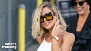 Khloe Kardashian wearing large square Gucci sunglasses and a white top, smiling outdoors.