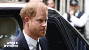 Prince Harry wearing a suit exiting a black car with blurred people in the background