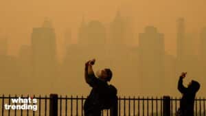 Two people wearing masks taking photos with a hazy, orange-tinted city skyline in the background