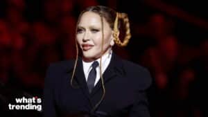 Madonna wearing a black suit and tie with braided hair styled in loops against a dark red background