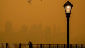 A person takes photos of the skyline as smoke from wildfires in Canada cause hazy conditions in New York City on June 7, 2023. An orange-tinged smog caused by Canada's wildfires shrouded New York on Wednesday, obscuring its famous skyscrapers and causing residents to don face masks, as cities along the US East Coast issued air quality alerts.
