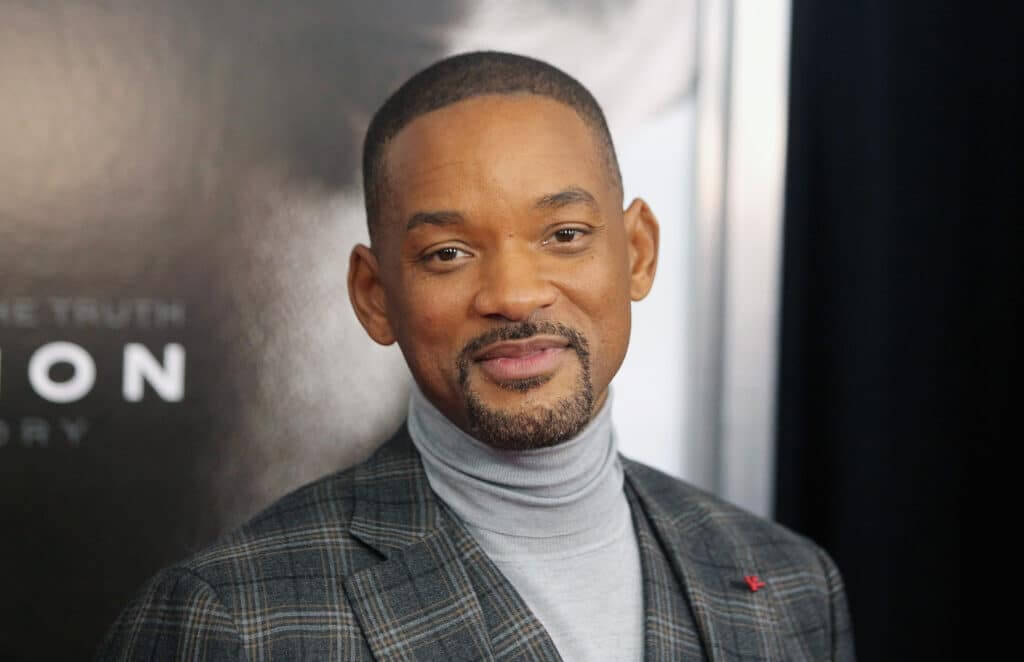 Will Smith wearing a gray turtleneck and plaid blazer at a movie premiere.