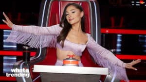 Ariana Grande sitting in a red chair on The Voice set wearing a lavender fringe crop top with arms outstretched.