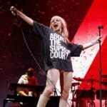 Singer Hayley Williams performing on stage wearing a black shirt with "ABORT THE SUPREME COURT" text