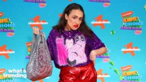 Miranda Sings wearing a purple cat sweater and red pants holding a silver bag at Nickelodeon Kids' Choice Awards 2023