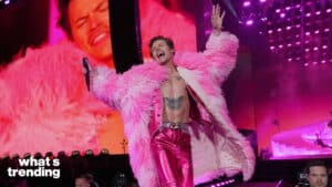 Harry Styles performing on stage wearing a pink feathered coat and shiny pink pants