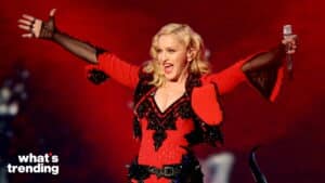 Madonna performing on stage in a red and black outfit holding a microphone with arms outstretched