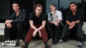 Four young men sitting on a bench, one wearing red and black striped pants, with "what's trending" text in the corner.