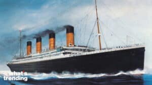 The RMS Titanic sailing with four smokestacks emitting black smoke against a blue sky