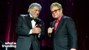 Tony Bennett and Elton John holding microphones on stage with red curtains behind them
