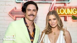 Man in light green blazer and woman in white striped dress posing in front of neon lounge sign