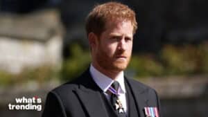 Prince Harry wearing a black suit with medals and a solemn expression outdoors