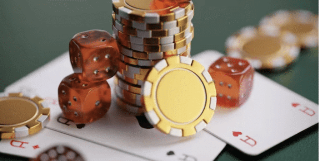 Stack of yellow and white poker chips, red dice, and playing cards showing queens on a green table.