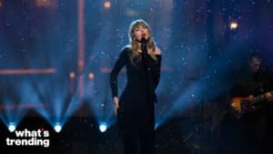 Taylor Swift singing on stage with snow-like effects and a guitarist in the background