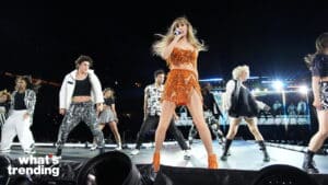 Taylor Swift performing on stage in an orange outfit with backup dancers during a concert.