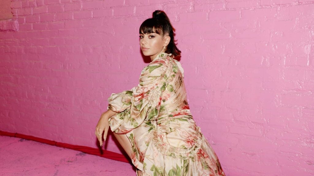 Charli XCX poses in front of a pink brick wall.