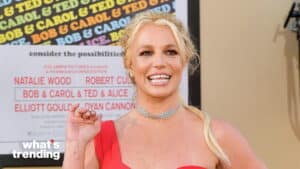 Britney Spears smiling and waving in a red dress at a movie premiere with a "Bob & Carol & Ted & Alice" poster background