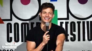 Young male comedian performing stand-up at a comedy festival, holding a microphone and smiling