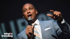 Man in a light blue suit speaking into a microphone with "what's trending" logo in the corner
