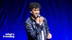 Man with curly hair and leather jacket speaking into a microphone against a blue background with "what's trending" text.