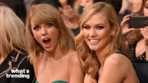 Taylor Swift with surprised expression and Karlie Kloss smiling at an event with audience behind them