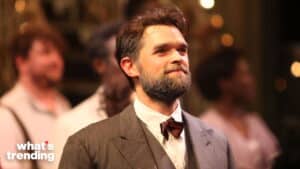 Man with beard and bow tie in vintage suit on stage with blurred people in background