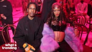 Rihanna showing her baby bump in a purple fur coat and headpiece sitting next to A$AP Rocky at an event.