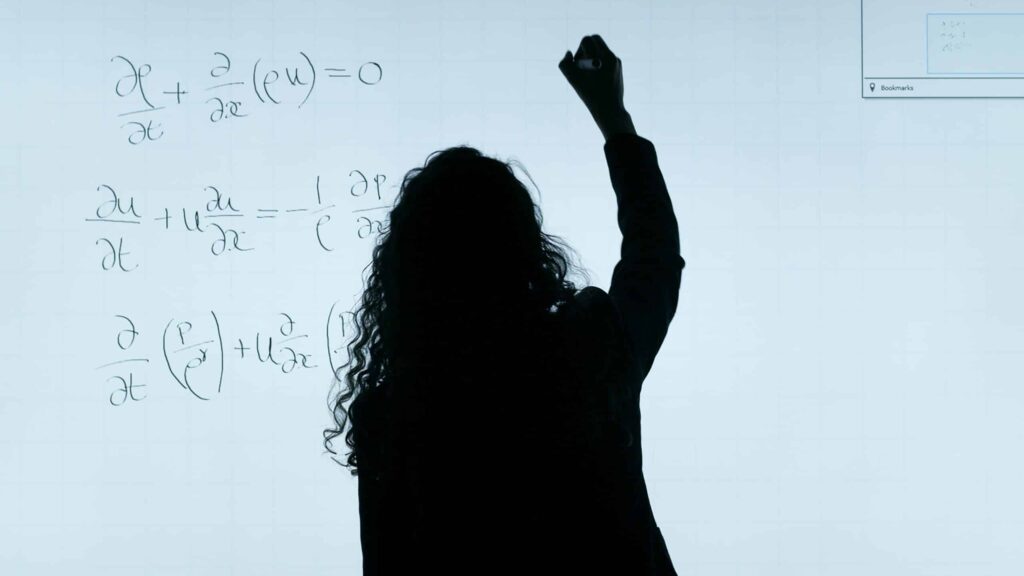 A woman stands in front of a whiteboard writing an equation. 