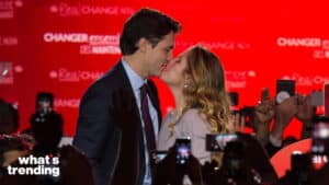 Justin Trudeau and Sophie Grégoire Trudeau kissing at a public event with a red backdrop and crowd taking photos