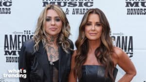 Two women posing at The Americana Music Honors & Awards, one with tattoos and a black leather jacket, the other in a black strapless top