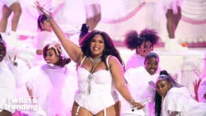 Lizzo performing on stage in a white corset with backup dancers in white outfits and pink lighting